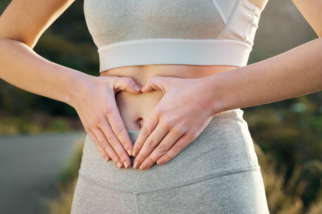 Woman with hands over stomach after tummy tuck by board certified cosmetic surgeon